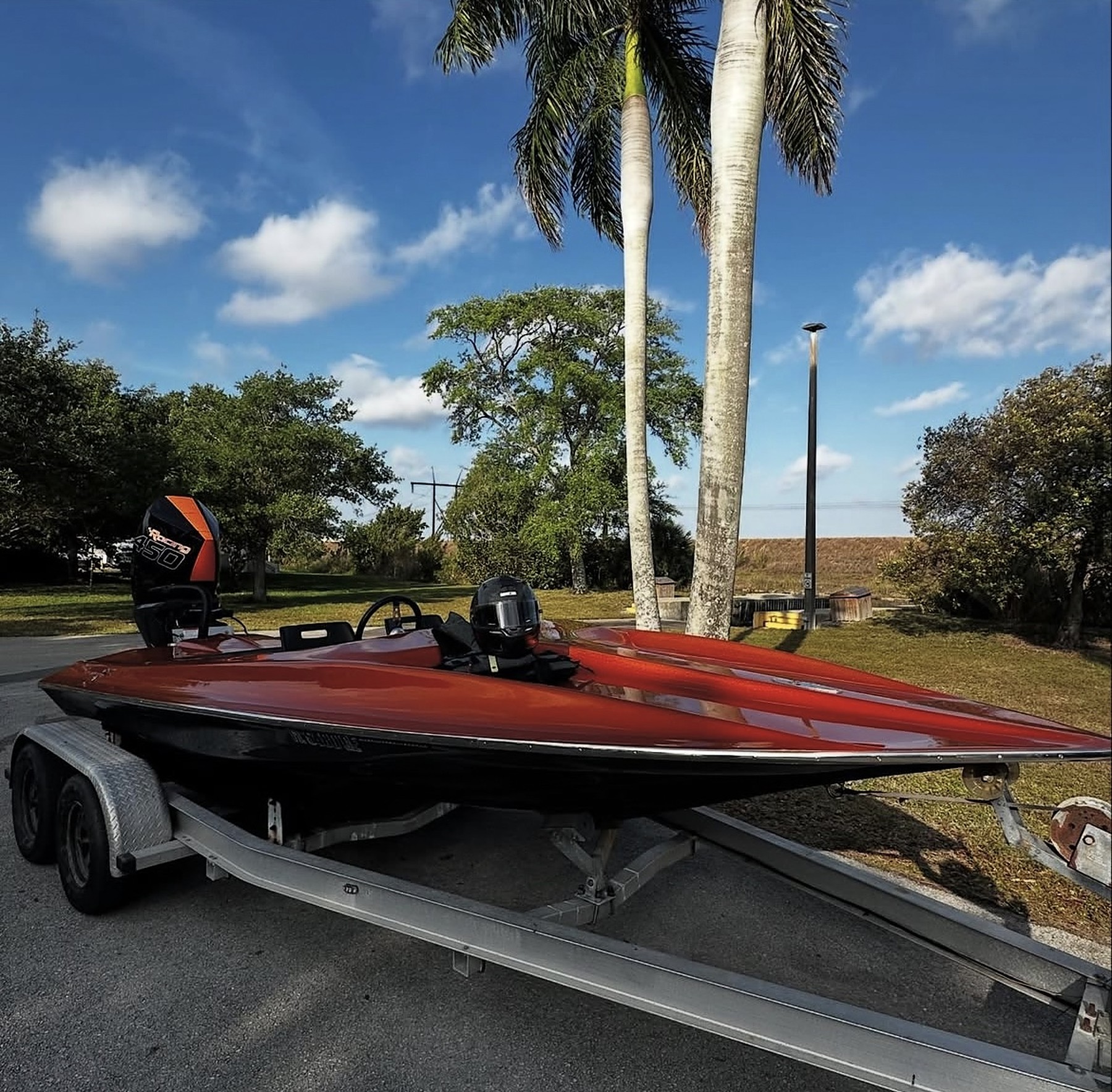 Candy-red racing boat with a mirror finish on a trailer under palm trees